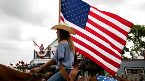 Getty Images Girl pictured in profile on a horse, wearing a cowboy hat and carrying an American flag