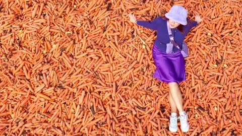 A student poses on 29 tonnes of carrots