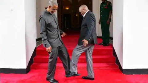 AFP Tanzanian opposition politician Maalim Seif Sharif Hamad (L) by tapping his feet against theirs to avoid themselves from coronavirus in Zanzibar, Tanzania on March 03, 2020.