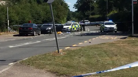 Police in Water Lane, Roydon. Police tape is visible and debris on the road