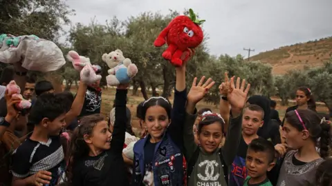 AFP Syrian children raise up toys that were given to them by a Syrian man living in Finland and calling himself "The Toy Smuggler"