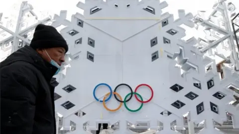 Reuters A man wearing a mask and coat walks past a building bearing the Olympics logo