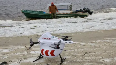 Drone Delivery Canada Drone sits on beach if front of a speed boat