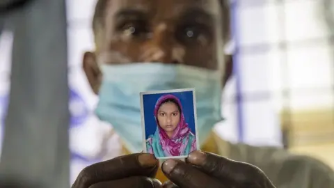 EPA A father holds a picture of his missing daughter at the Dhaka Medical College Hospital in Dhaka, Bangladesh, 10 July 2021