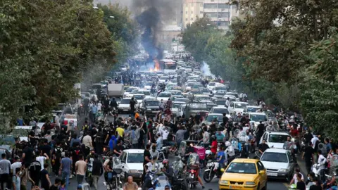 Getty Images Dozens of people protest over the death of a woman in policy custody with lots of cars and fires on street.