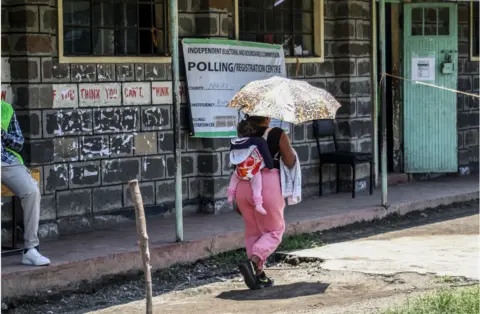 Getty Images Woman with an umbrella with her baby on her back walking on the road.