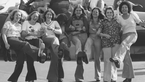 Liverpool John Moores University Littlewoods ladies posing for photo with ride in background, Littlewoods outing in Blackpool. 1973