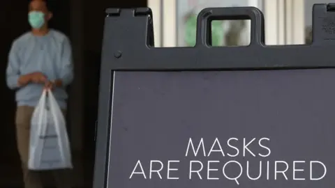 Los Angeles Times via Getty Images A sign tells store customers to wear masks to prevent the spread of Covid-19