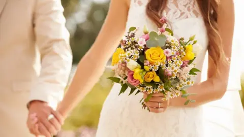 iStock / Getty Images A stock picture of an unidentified straight couple holding hands at their wedding