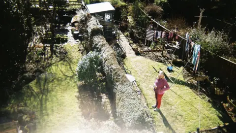 Chris Ruskin Photo taken from upstairs window showing woman standing alone in a back garden