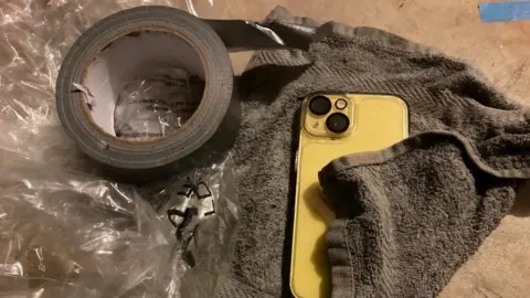 Martin Heath/BBC A smart phone partially wrapped in a towel with tape to seal the package