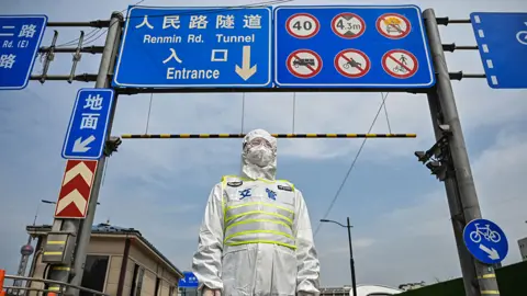 Getty Images A transit officer, wearing a protective gear, controls access to a tunnel in the direction of Pudong district in lockdown as a measure against the Covid-19 coronavirus, in Shanghai on March 28, 2022