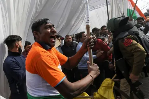 Reuters A man, from the group which raised the anti-farmers slogan, shouts as he holds a stick, at a site of the protest against farm laws at Singhu border near New Delhi, India January 29, 2021.