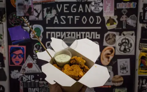 BBC A box of tofu-seitan nuggets being held up in front of the sign for Horizontal