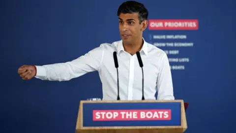 Reuters Rishi Sunak at a podium which reads "Stop the boats"