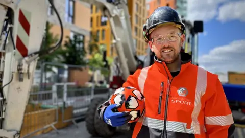 A worker on a building site with a football