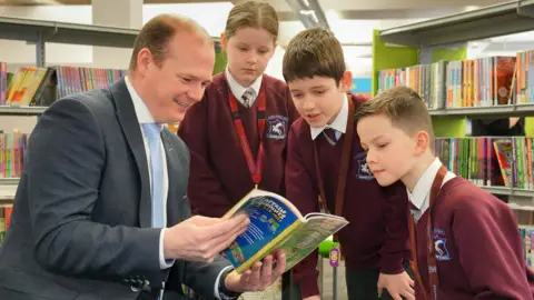 Aaron McCracken Communities Minister Gordon Lyons with pupils from Largymore Primary School as they celebrate World Book Day at Lisburn Library