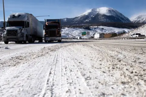 JASON CONNOLLY/AFP Semitrucks line up in the eastbound land on I-70 in Silverthorne, Colorado on December 22, 2022.