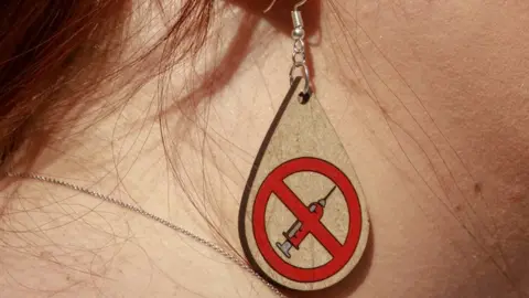 Getty Images Anti-vax earring with a logo of a vaccine crossed out.