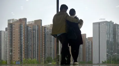 Getty Images A couple look out of a window at blocks of flats in Beijing