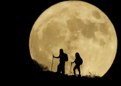 BORJA SUAREZ/Reuters Women walk up a mountain with the full moon known as the "Sturgeon Moon" in the background, in Arguineguin, in the island of Gran Canaria, Spain, August 1, 2023.