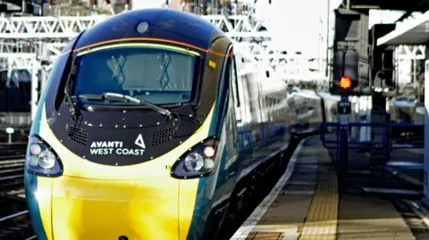 A close up shot of an Avanti train which is facing towards the camera next to a platform. It has a yellow front and turquoise sides.