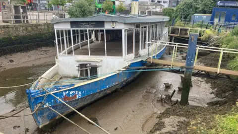 A derelict boat sits on the silt in. riverbed.