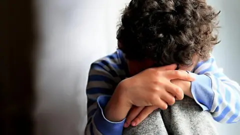 Getty Images A boy sat down with his head at his knees with his face not visible.
