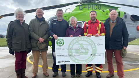 Anna Connell holding a giant cheque with members of the DSAA in front of a helicopter
