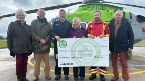 Anna Connell holding a giant cheque with members of the DSAA in front of a helicopter