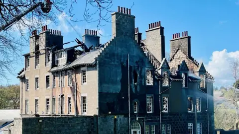 Firefighters in a height vehicle using water to dampen down the shell of a building hit by fire.