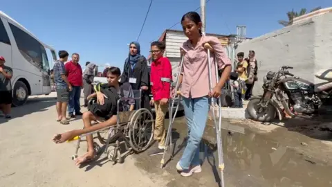 Sarah Marzouk, die op krukken loopt nadat ze haar voet heeft verloren, wacht met een groep mensen (30/07/24)