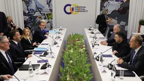 AFP via Getty Images The leaders sit at two tables facing one another, with microphones and documents on the table in front of them 