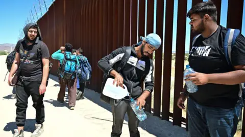 Getty Images Migrants from India's Punjab region pause for water while walking beside the US-Mexico border wall at at Jacumba Hot Springs, California on June 5, 2024.