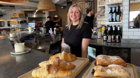 A photo of Nia Roberts behind the bar of her restaurant - croissants and pastries in the foreground, staff members in the background