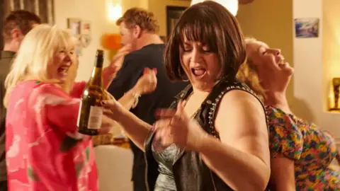 BBC/Toffee International Ltd./Tom Jackson Ruth Jones as Nessa holding a botttle and dancing in Gavin and Stacey Christmas Special 2024