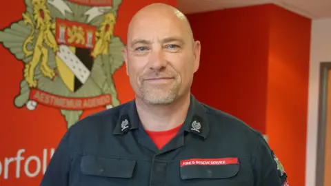 Shaun Whitmore/BBC Paul Seaman has a greying beard and is wearing a uniform that says Fire and Rescue Service.