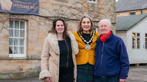 Gala Kononenko Tali Michaels, Chair of Trustees at Michael Hall, Jessika Hulbert, Chair of Wealden District Council and former Michael Hall student Stephen Sheen were among the attendees. Tali, on the left, is wearing a long beige coat with puffed collar and sleeves. Jessika, in the middle, is wearing a blue/green tartan skirt and yellow jacket. Stephen, on the right, is wearing navy trousers, a royal blue jacket and navy trousers. 