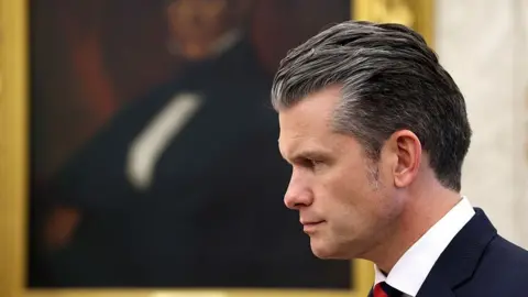 Pete Hegseth in profile in the Oval Office. Out of focus in the background is a portrait in a gold frame. 