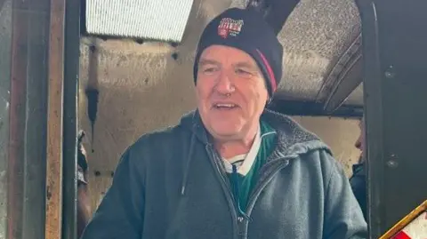 Family handout Martin Sullivan, smiling, wearing a dark hat, dark hoodie and top, and standing in the doorway of an old train carriage. 