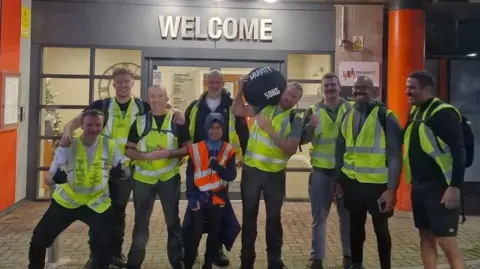 Group of men at the end of their charity walk outside Blackpool FC's Bloomfield Road carrying a sandbag 