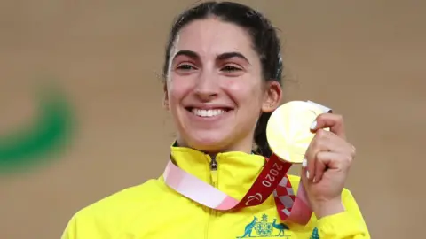 Paige Greco, in a bright yellow Team Australia jacket, poses with her gold medal at the Tokyo 2020 Paralympic Games in Izu, Japan