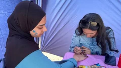 A woman doing Henna on another woman inside a marquee at a festival