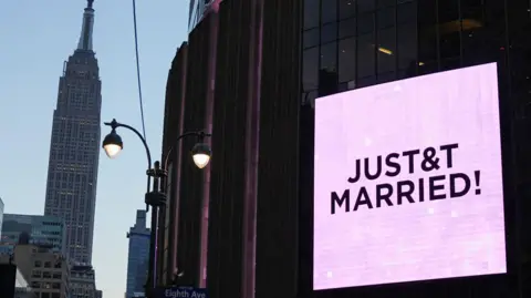 Pink screens outside Madison Square Garden showing New York in the twilight, with Empire State Building in the background