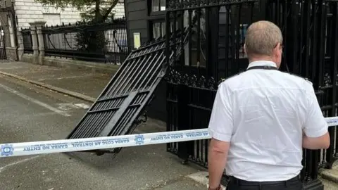 RTÉ Man stands at police cordon in front of damaged gates 