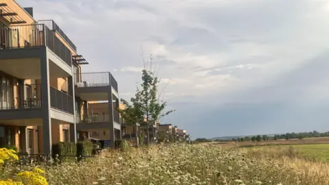 A row of modern apartment blocks overlooking green fields and meadows.