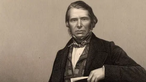 Getty Images Sepia Image of Charles Edward Trevelyan, looking directly, with sideburns, cravate, checked waistcoat and jacket, holding a book