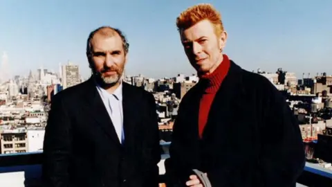 Changes: Bowie At Fifty - Picture shows Alan Yentob (left) and David Bowie. Yentob. The pair, both wearing black suits, are pictured with the London skyline behind them.