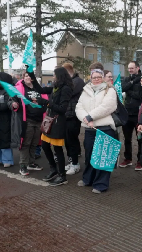 Teachers stood with banners outside a school