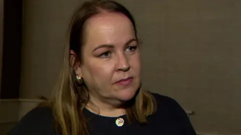 Joleen Cunningham has medium-length blond/brown hair and is wearing a dark buttoned up top